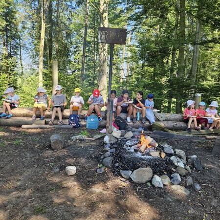 Kinder sitzen im Wald ums Feuer